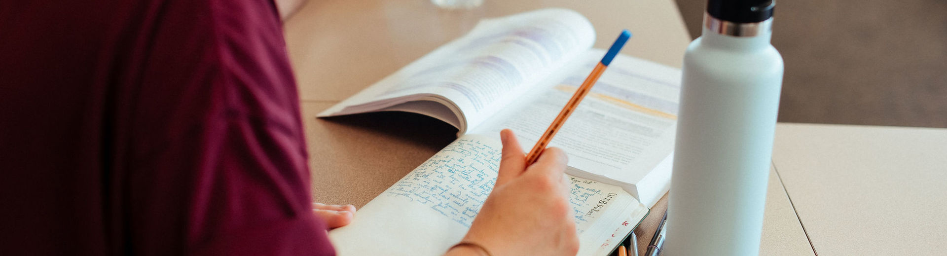 Female student is diligently taking notes while reading a highlighted text book.