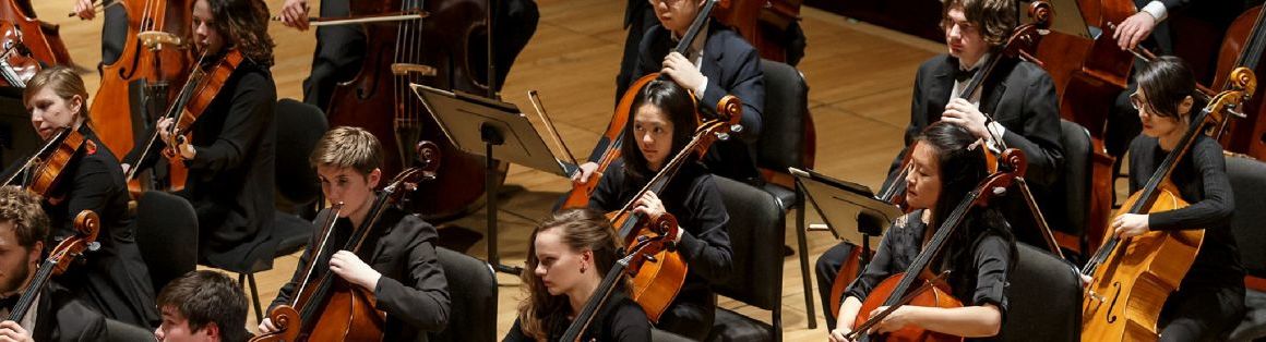 A student string orchestra is shown mid-performance. All musicians are dressed in formalwear.
