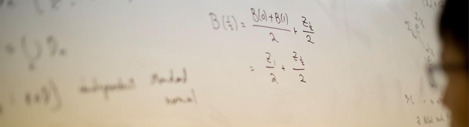 Student writing math equation on white board in a College of Science and Technology classroom.