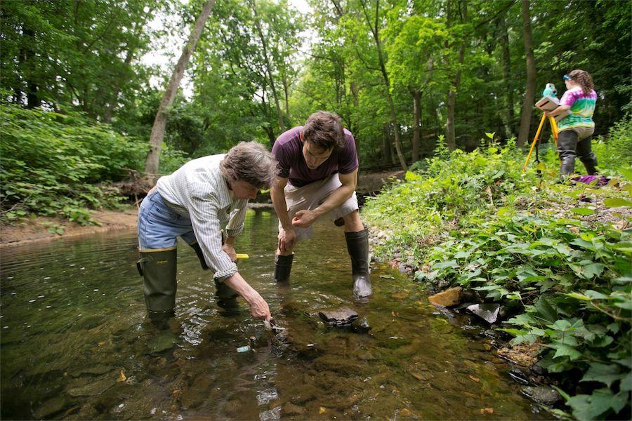 Two environmental science students wearing waders and standing in a stream to test water.