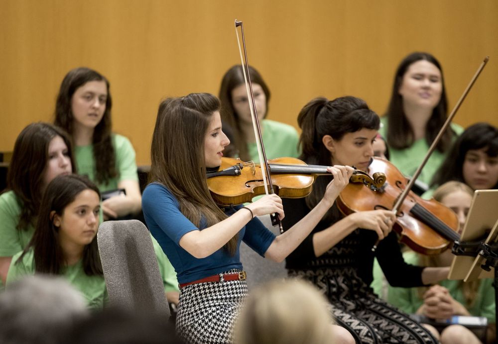 Two women play violin for students.