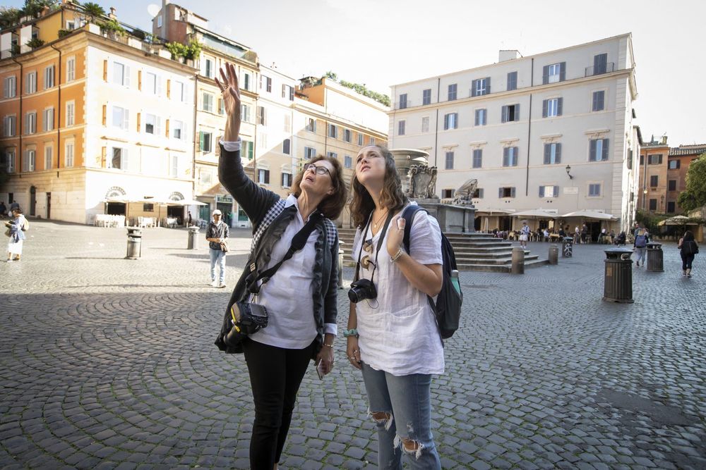 A professor and student with cameras around their necks observe their surroundings in an Italian piazza.