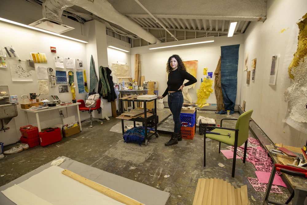 A student in black clothing paints in an art studio. 