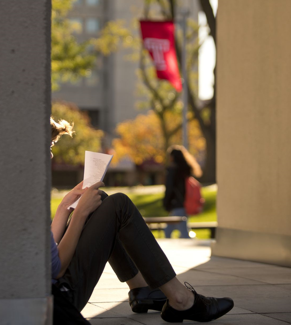 A student sits in the shade on a sunny afternoon, reading a packet of papers